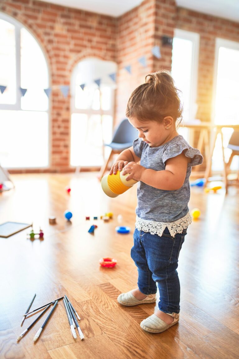 A young child using colorful playdough and child-safe scissors at a table with paper and crayons.